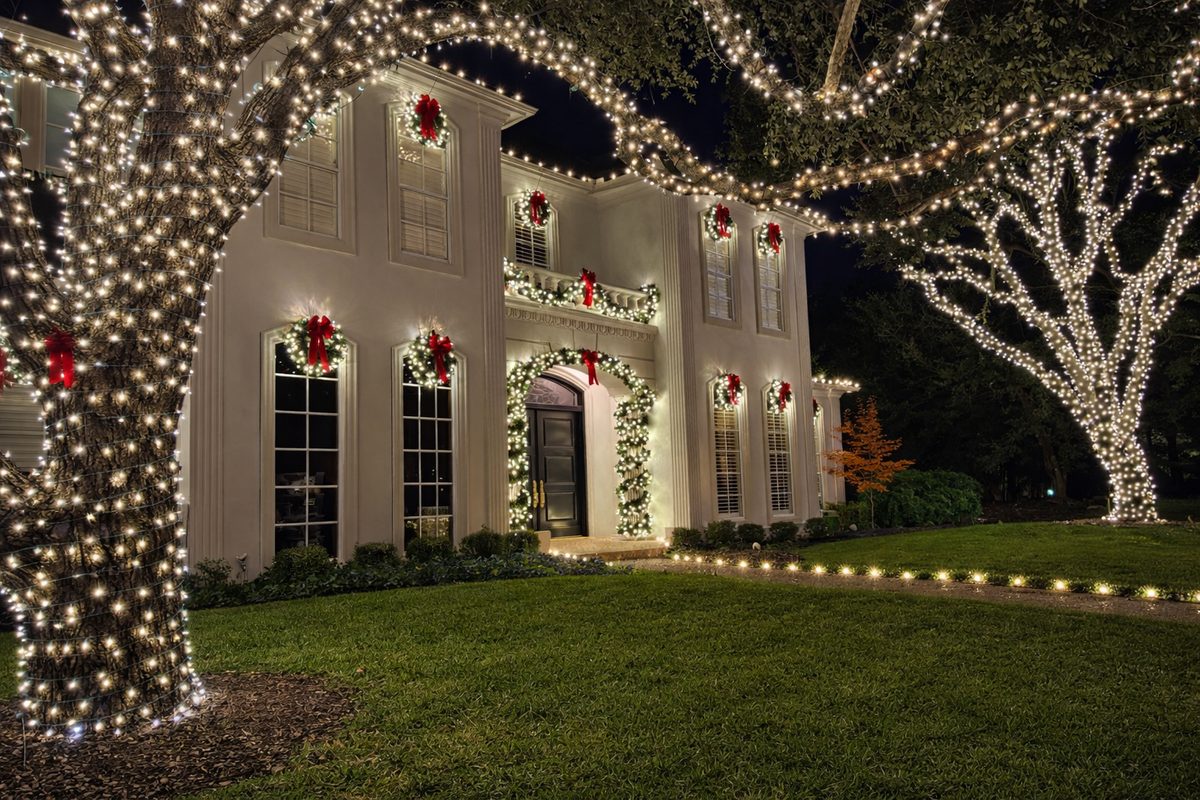 Warm-white holiday lighting on trees and the home for Dallas luxury homes