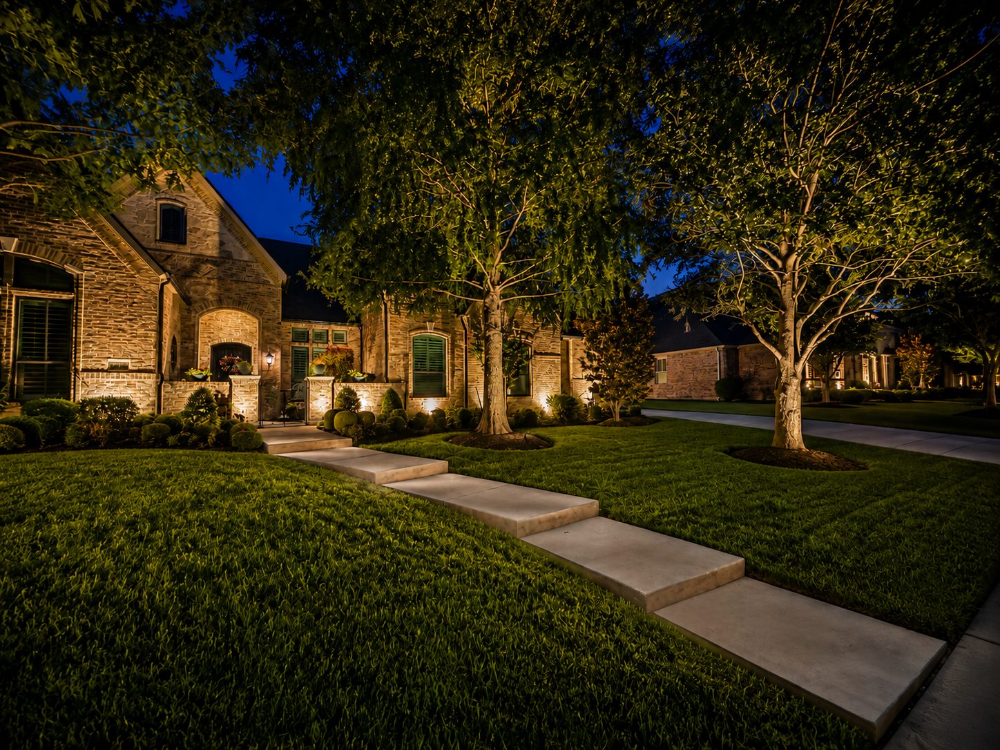 Arched front of a stone and brick home with architectural lighting and tree uplighting