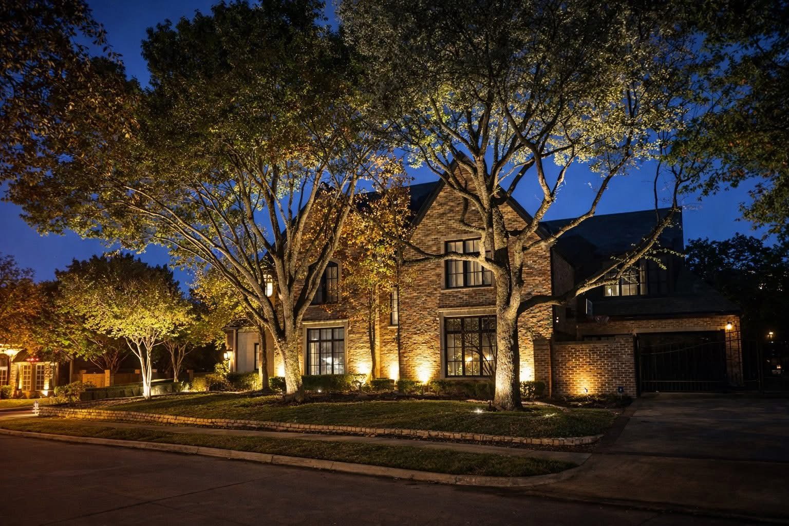Architectural lighting on a two-story brick home, with tree uplighting