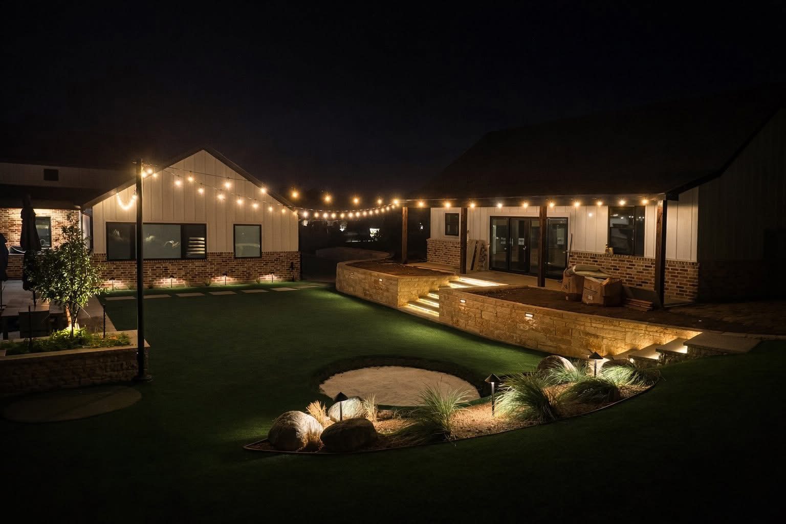 Bistro lighting with string lights over a courtyard, a stone planter, and turf
