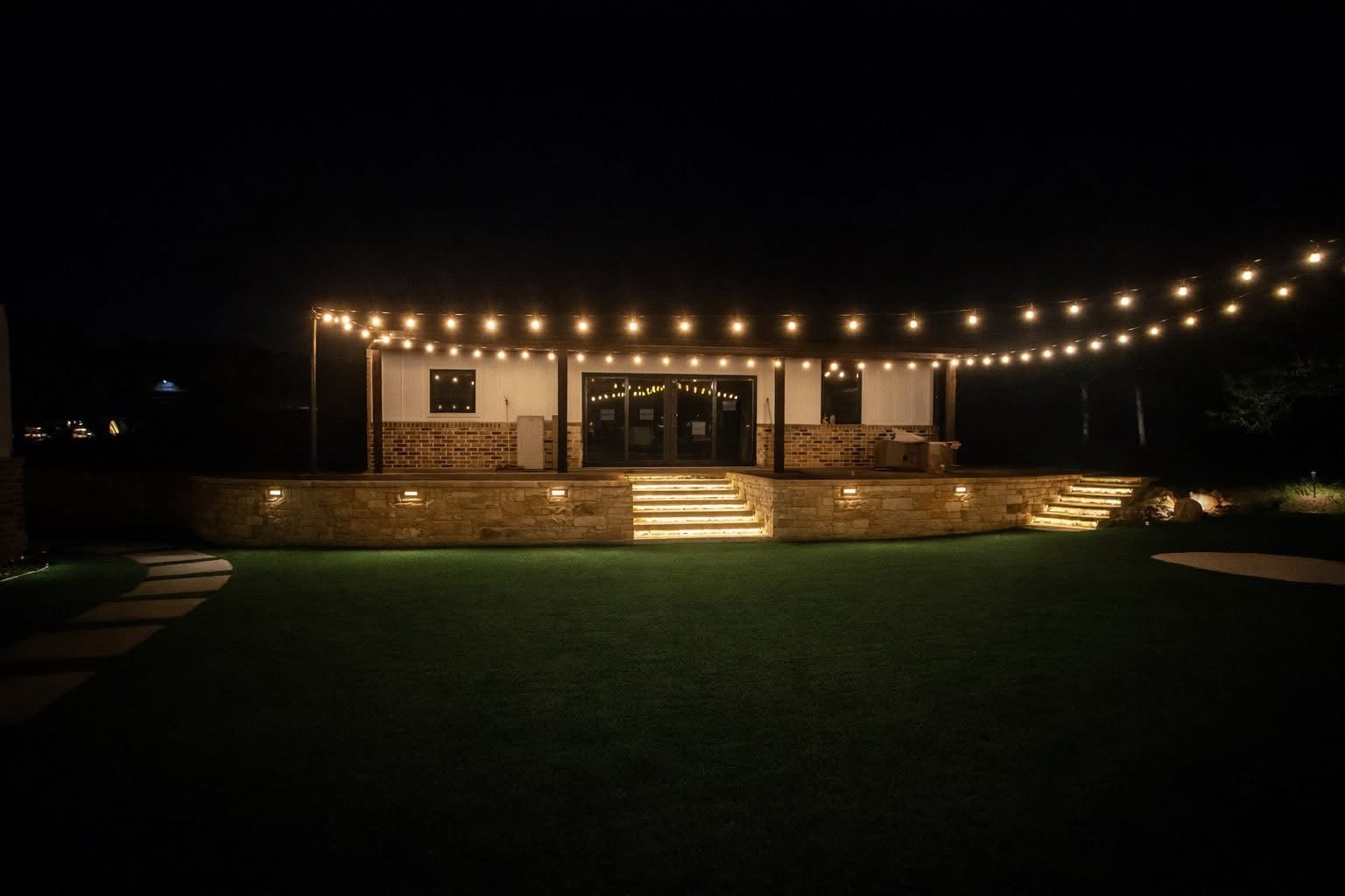 Strip lighting in stone steps under bistro string lights on a covered patio