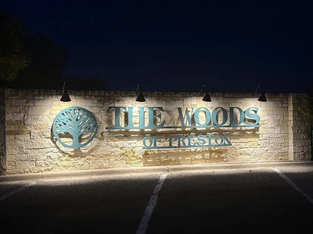 Commercial lighting on the stone monument sign that reads The Woods of Preston