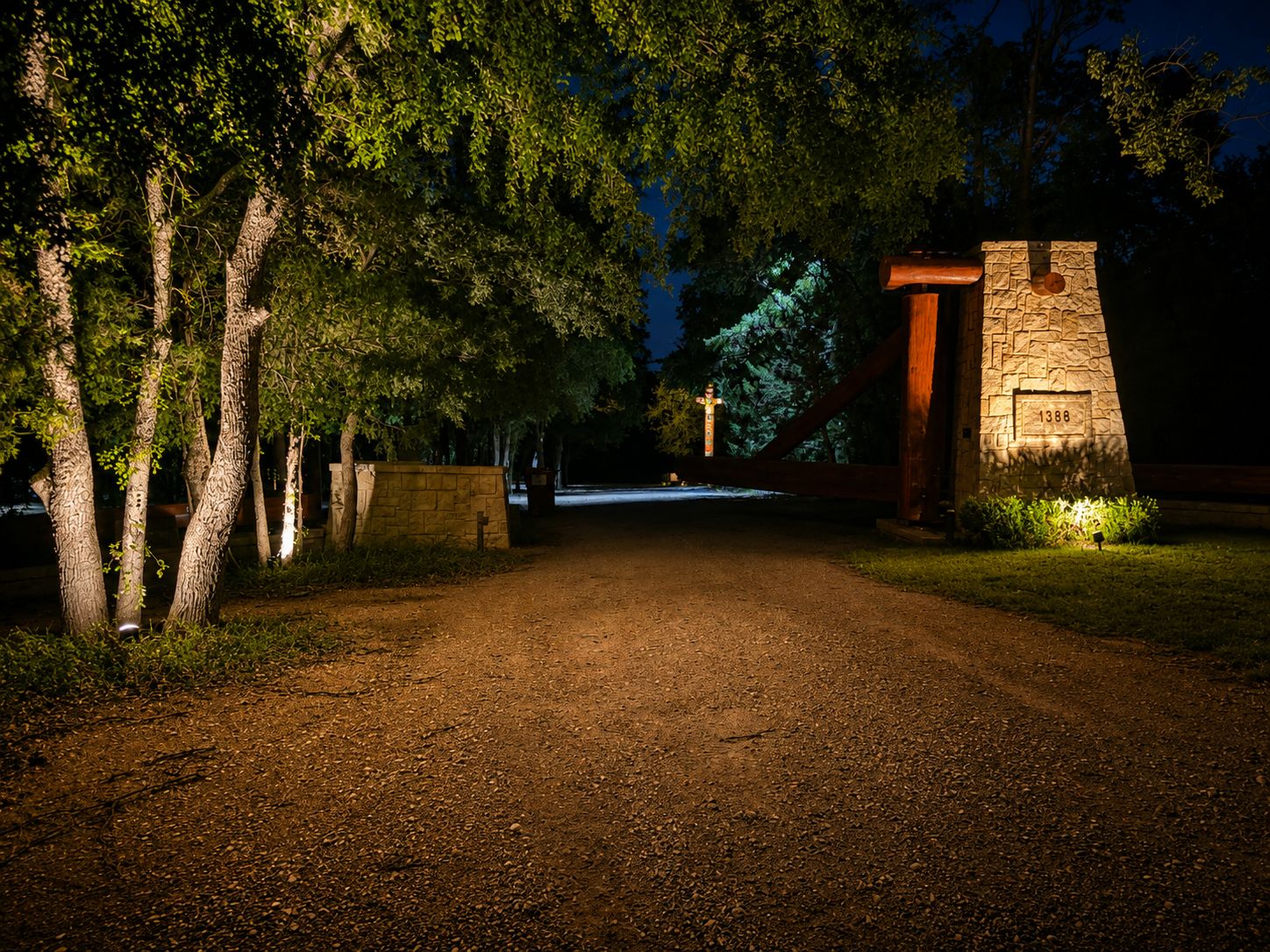 Night lane toward a stone entry pier, with path lights and tree uplighting
