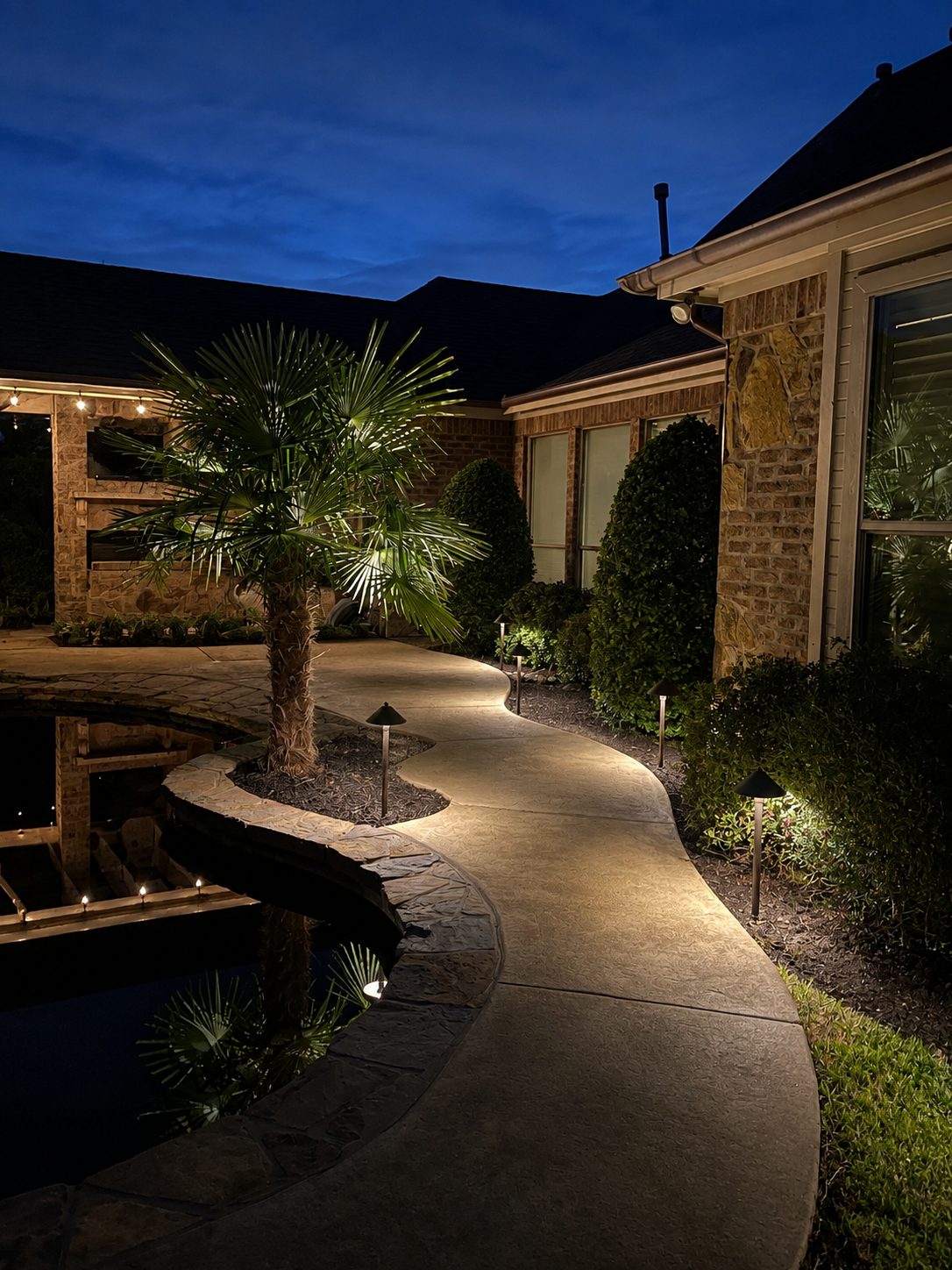 Curved walkway by a pond with a palm and path lights