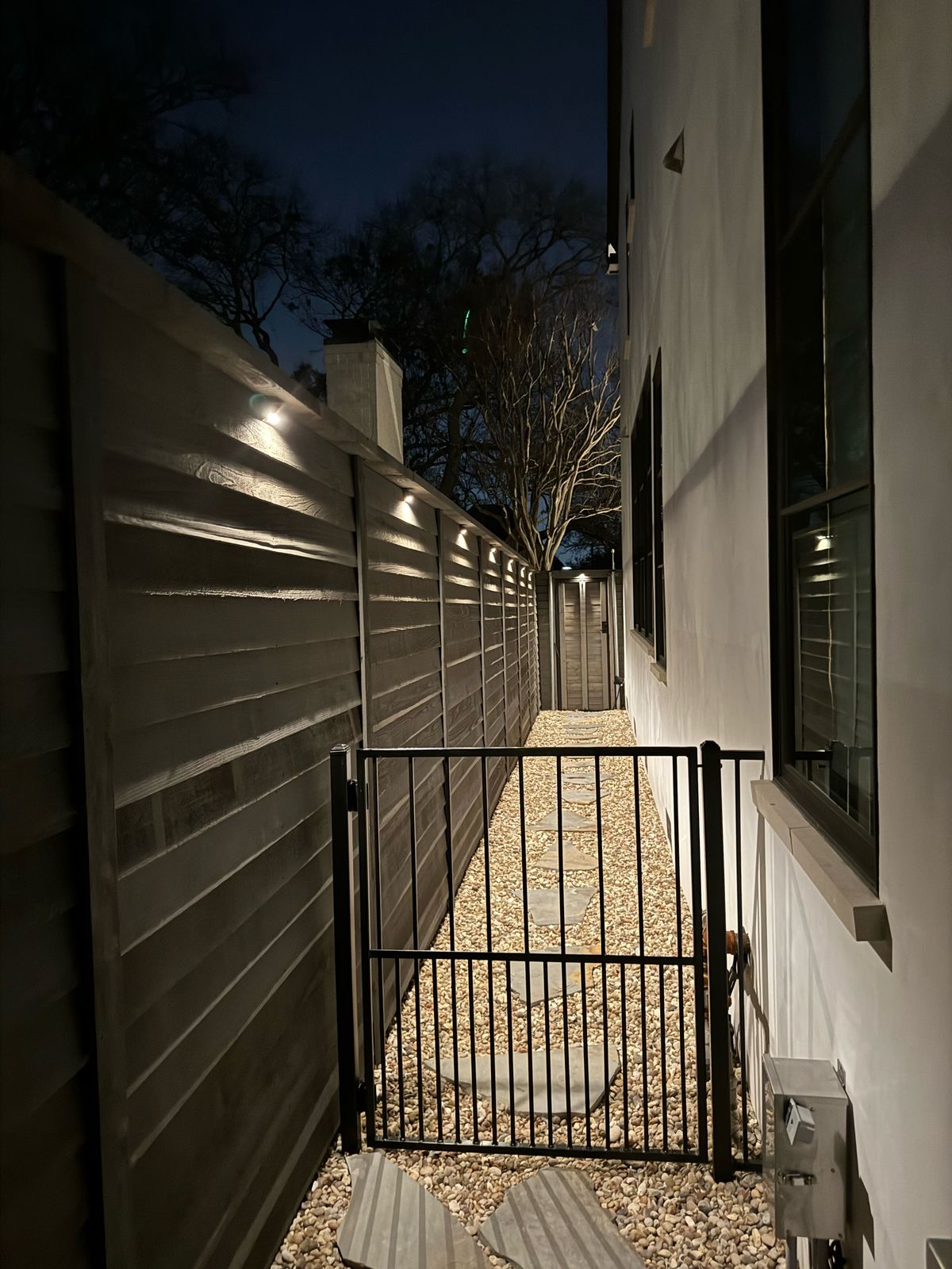 Security lighting in a narrow side yard, with a fence, a gate, and a wall wash