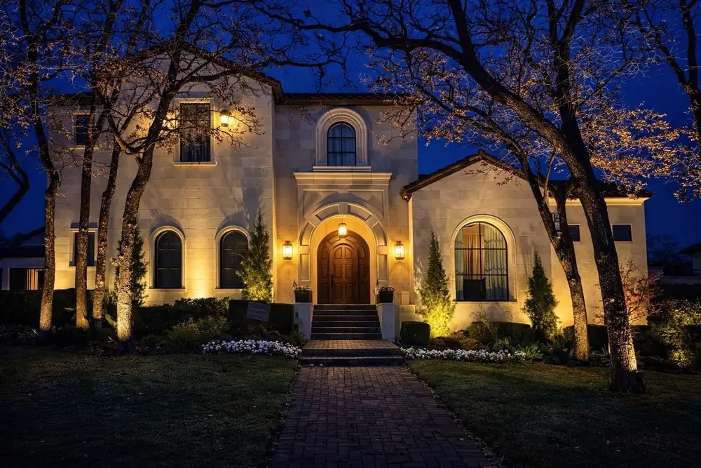 Stone entry at night with architectural lighting on the stone, an arched door, and tree uplighting