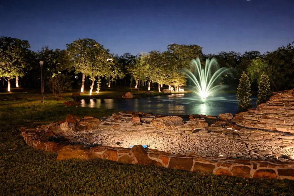 Tree uplighting around a pond, with a lit fountain