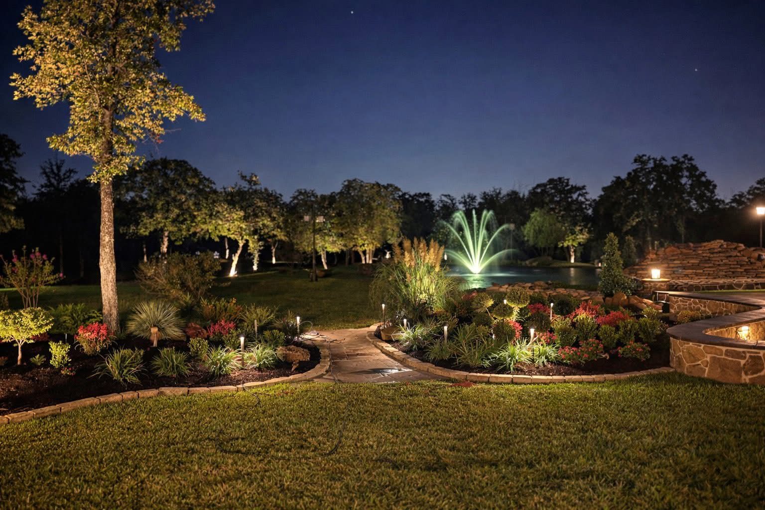 Garden path toward a fountain and pond, with tree uplighting