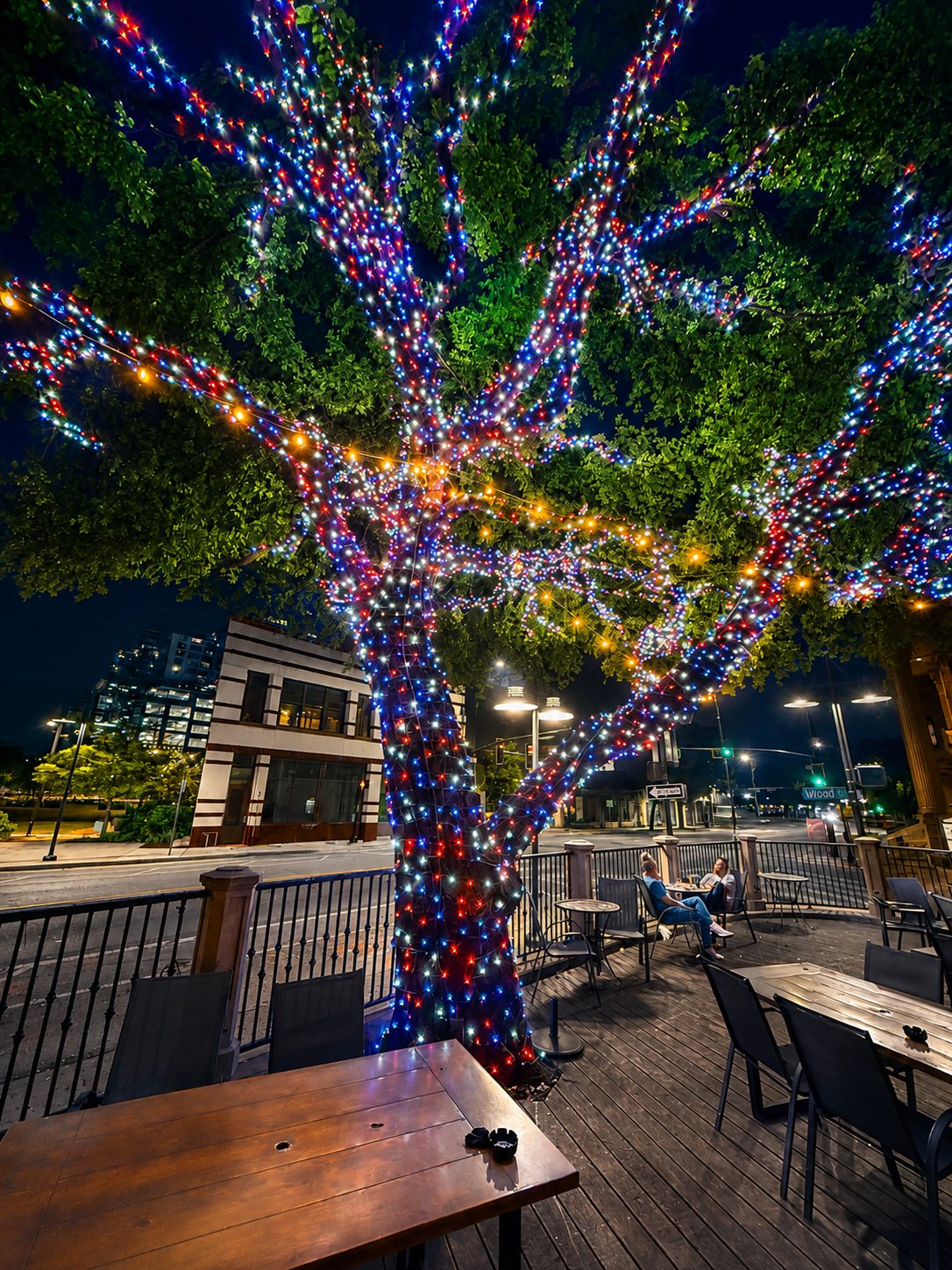 Large tree wrapped in multicolor lights on an outdoor dining patio