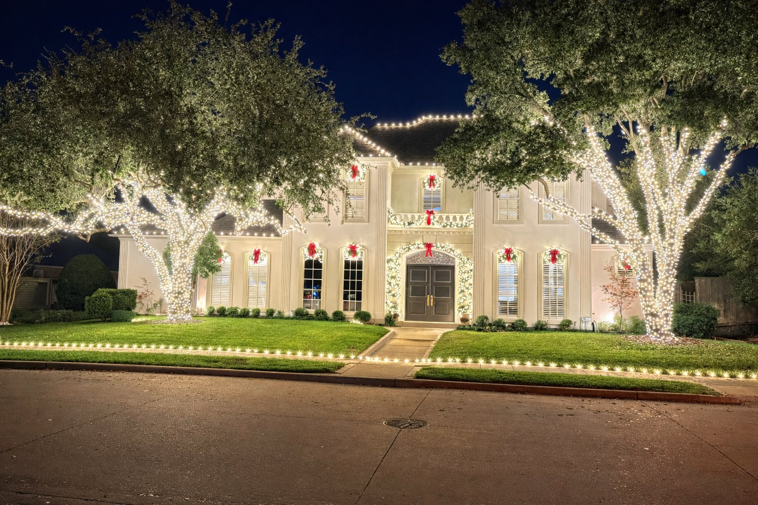 White two-story home with wrapped trees, red bows, and roofline Christmas lights
